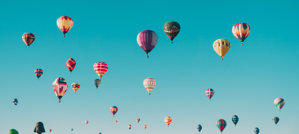 hundreds of colourful hot air balloons rising against a clear blue sky